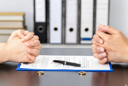 Two pairs of hands with rings on table and paper with pen