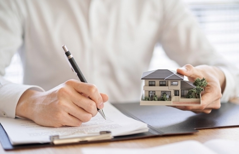 Person with house in hand and pen with paper